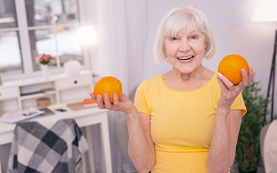 Elderly woman in yellow shirt holding 2 oranges